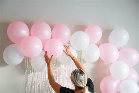 A Woman Reaching Up To Some Pink And White Balloons In Front Of A Wall