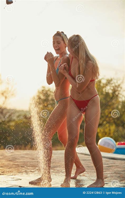 Two Female Friends Sharing Outdoor Shower By The Swimming Pool Stock