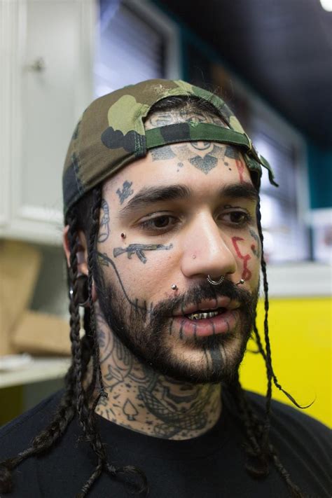 A Man With Tattoos On His Face And Beard Is Looking At The Camera While