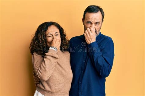 Middle Age Hispanic Couple Wearing Casual Clothes Smelling Something Stinky And Disgusting