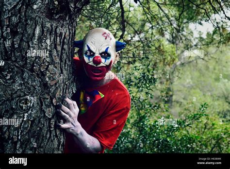 Closeup Of A Scary Evil Clown In The Woods Emerging From Behind Of A