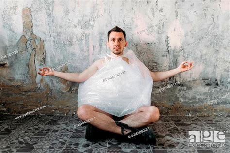 Funny Freak Man Wrapped In Packaging Film Sitting In Yoga Pose Grunge Room Interior Stock