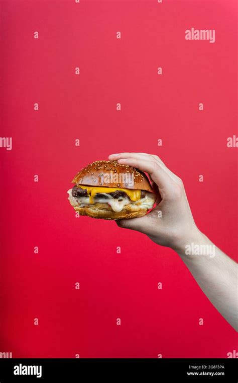 Human Hand Holding Tasty Hamburger Cheeseburger Burger Isolated On Red Background Stock Photo
