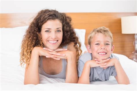 Cheerful Mother And Son Lying On Bed Looking At Camera Stock Photo