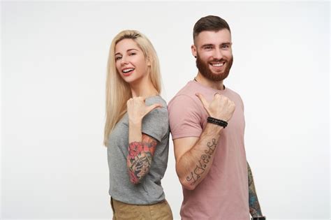 Веселая молодая прекрасная пара с татуировками показывает друг на друга