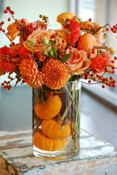 A Vase Filled With Lots Of Orange Flowers And Pumpkins