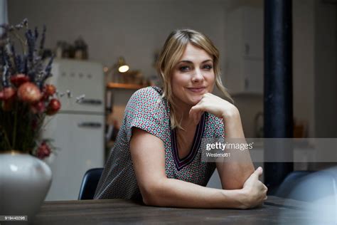 Portrait Of Smiling Woman Sitting At Table In The Kitchen High Res