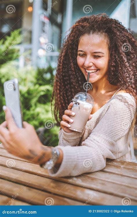 Young Smiling Afro Haired Woman Take Selfie With White Smartphone Sitting At The Cafe Outside At
