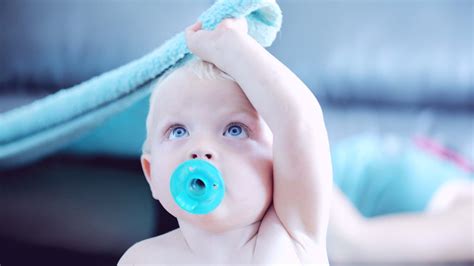 Blue Eyes Baby Toddler With Pacifier In Mouth Is Sitting In Blur