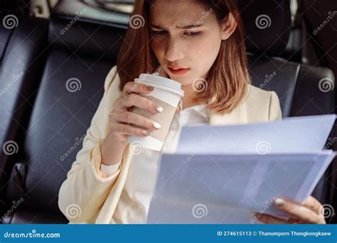 Businesswoman Sitting In The Back Seat Of The Car With A Paperwork In Her Hand And Drinking