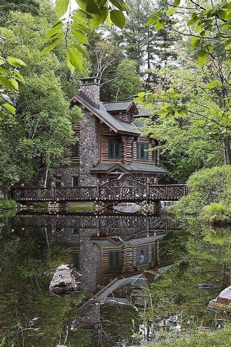 A Log Cabin In The Woods With Water And Trees Around It Surrounded By Greenery