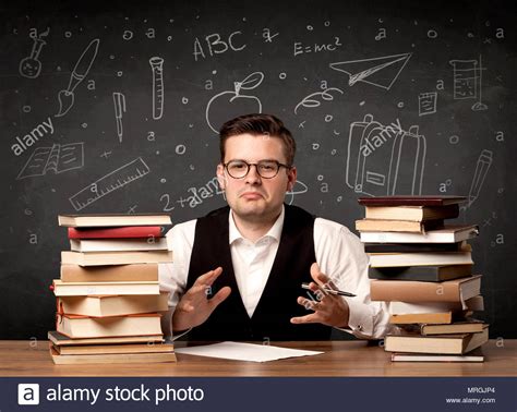 A Passionate Young Teacher Sitting At School Desk With Pile Of Books In