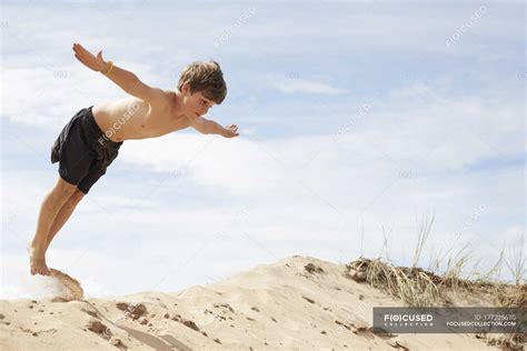 Boy On Beach Dune Jumping Into The Air With Outstretched Arms