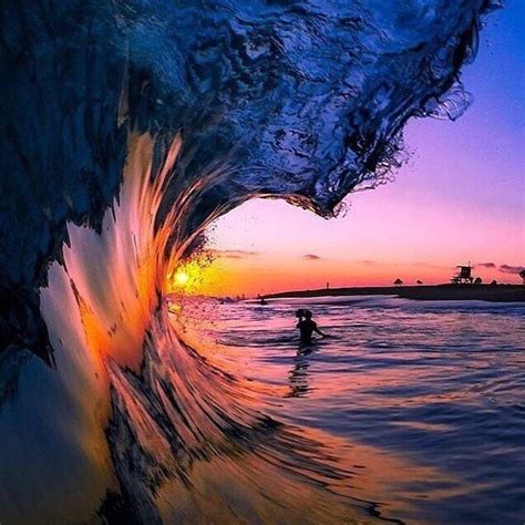 A Man Riding A Wave On Top Of A Surfboard Under A Purple And Blue Sky