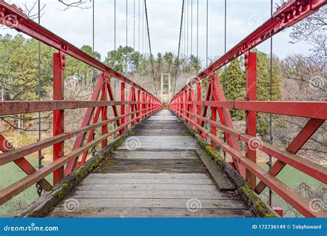 Winter View Of Red Suspension Footbridge Over Lake In Forest Valley In