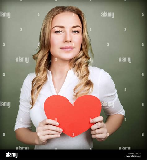 portrait of cute loving woman holding in hands red paper heart isolated on gray background