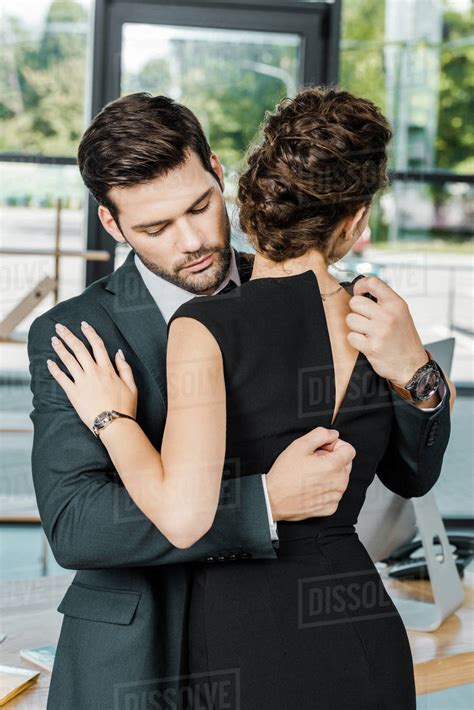 Young Businessman Unzipping Dress Of Seductive Businesswoman At