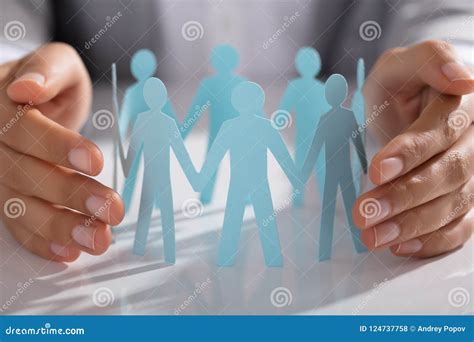 Businessperson Hand Protecting Paper Cut Out Figure On Table Stock