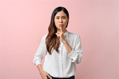 an asian woman covers her mouth with her hand standing on pink isolated background stock image