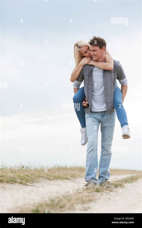Full Length Young Man Giving Piggyback Ride Woman On Trail Field Stock