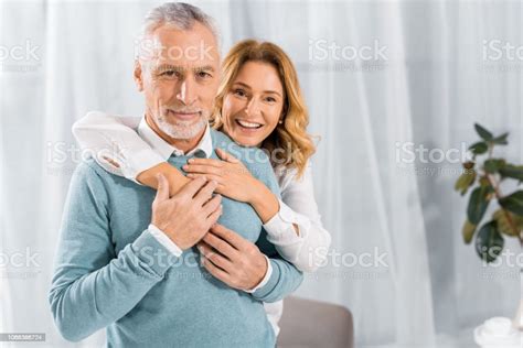 Beautiful Happy Wife Embracing Mature Husband From Behind At Home Stock