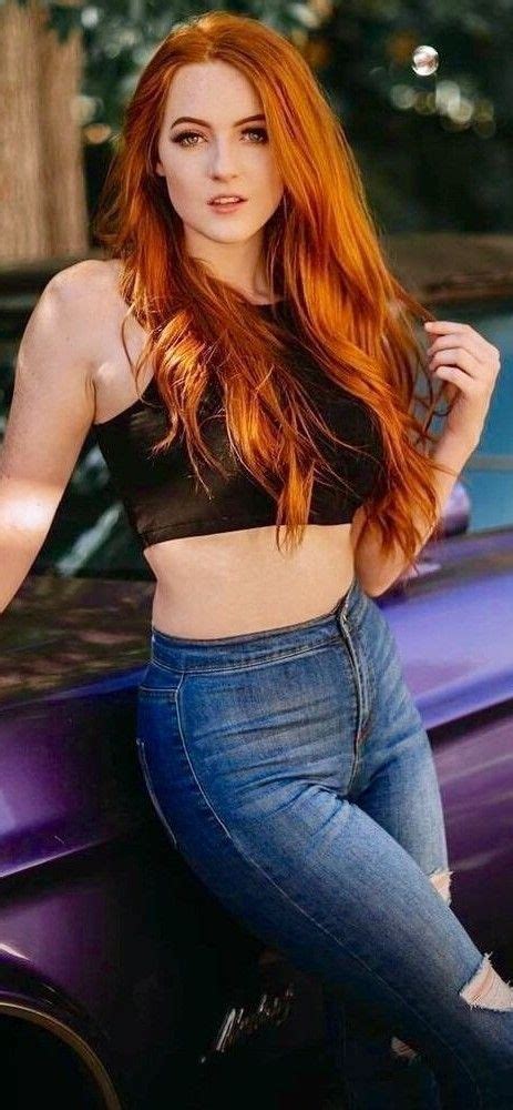 A Woman With Red Hair Is Leaning On The Hood Of A Car And Posing For A