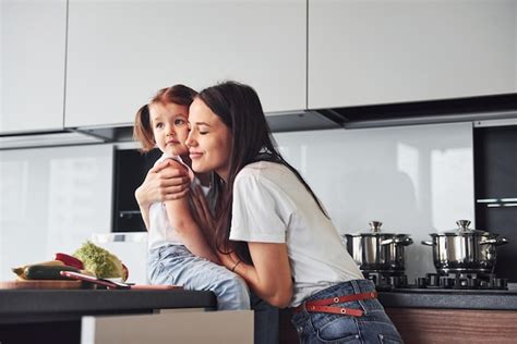 Mãe com sua filha abraçando se dentro de casa na cozinha Foto Premium