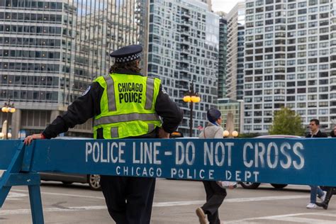 A Chicago Police Officer Stands Next To A Large Blue Barrier With Police Line Do Not Cross