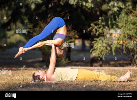 Young Couple Doing Acroyoga Exercises In Park Man Holding Woman On