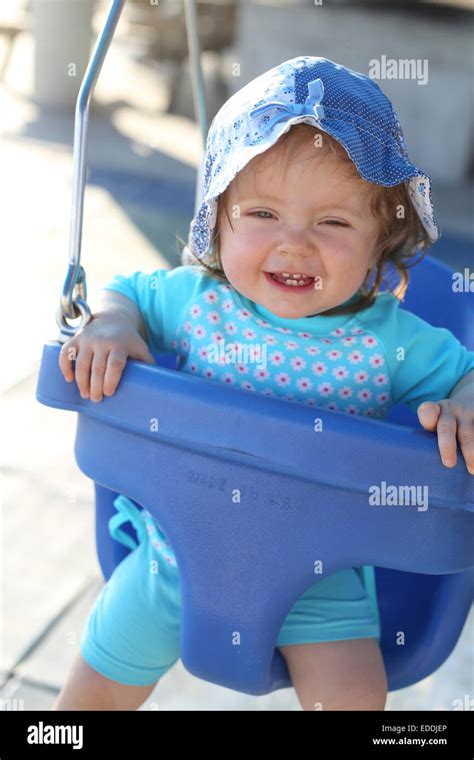 Portrait Of Smiling Baby Girl Sitting On Blue Baby Swing Stock Photo