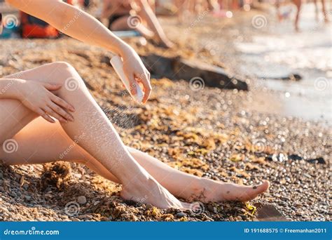 A Woman Sitting On The Beach By The Sea Sprays Cosmetics On Her Feet