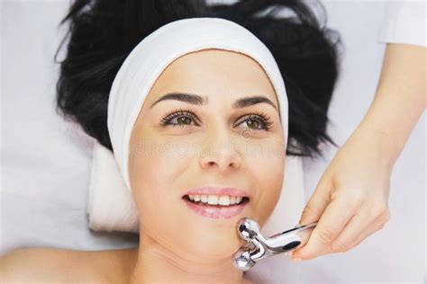 Professional Cosmetologist Using Facial Roller Massage Instrument To Make Rejuvenation Face