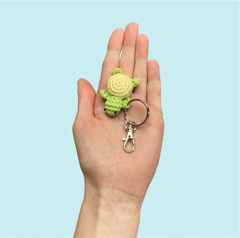 A Hand Holding A Keychain With A Crocheted Turtle On It