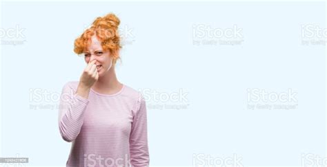 Young Redhead Woman Smelling Something Stinky And Disgusting Intolerable Smell Holding Breath
