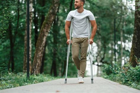Walking In The Beautiful Park Man With Crutches Is Outdoors Stock