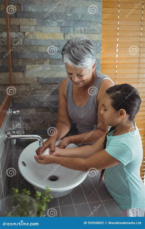 Grandmother And Granddaughter Washing Hands In Bathroom Sink Stock