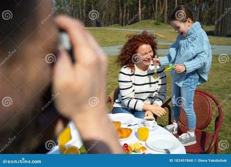 Man Photographing His Cheerful Wife And Daughter Outdoors Stock Photo