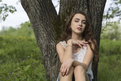 A Girl With Long Hair Sits By The Trunk Of A Tree Stock Photo Image