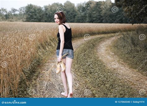 Young Girl Walking Barefoot On The Ground Road Through Field And Forest