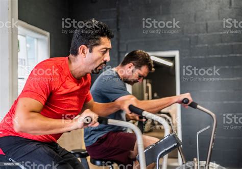 Two Mature Men Latino And Caucasian Doing Cycling Exercise In The Gym