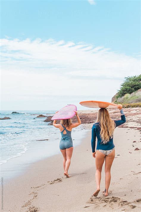 Two Women Walking On The Beach Carrying Surfboards On Their Heads