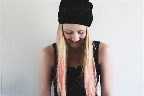 laughing teen girl with long blonde and pink hair is wearing a black beanie by stocksy