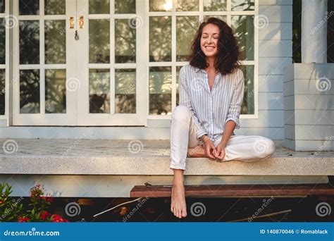 Portrait Of A Beautiful Happy Young Woman Sitting On The Porch Of Terrace With Her House On