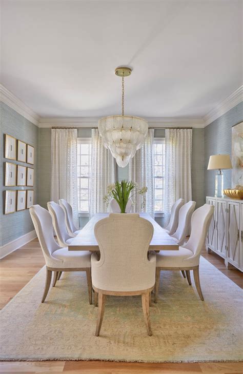 A Dining Room Table With White Chairs And A Chandelier