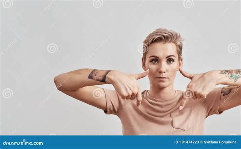 Look Here Portrait Of Tattooed Woman With Pierced Nose And Short Hair In Beige T Shirt Looking
