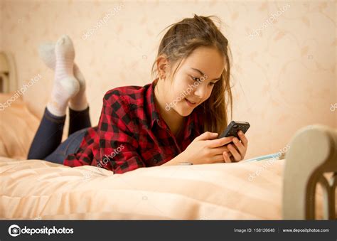 Portrait Of Cute Teenage Girl Lying On Bed And Typing Message On Stock