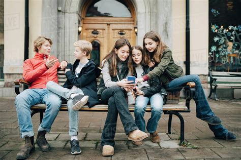 Male And Female Friends Talking While Sitting On Bench In City Stock