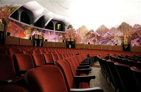 An Empty Auditorium With Red Seats And Large Murals On The Wall Behind