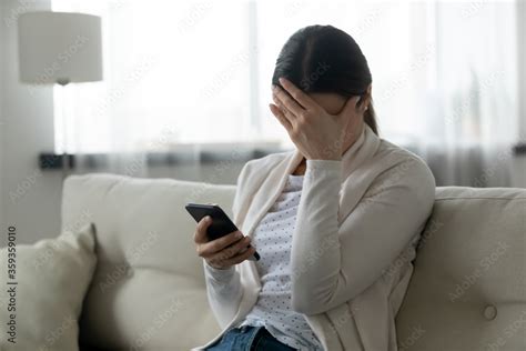 Woman Sit On Sofa Holding Smartphone Cover Face With Hand Feels Scared