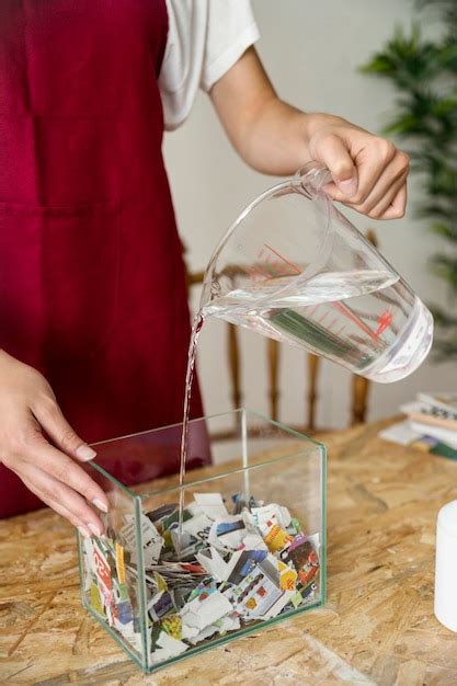 Close Up Of A Womans Hand Pouring Water On Torned Paper In Container